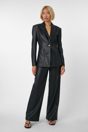 Woman wearing a black vegan leather suit on a light grey background