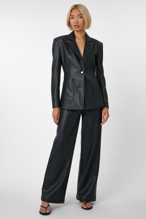 Woman wearing a black vegan leather suit on a light grey background