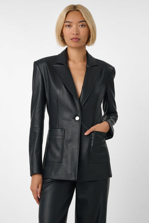 Woman wearing a black vegan leather suit on a light grey background