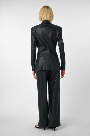 Woman wearing a black vegan leather suit on a light grey background