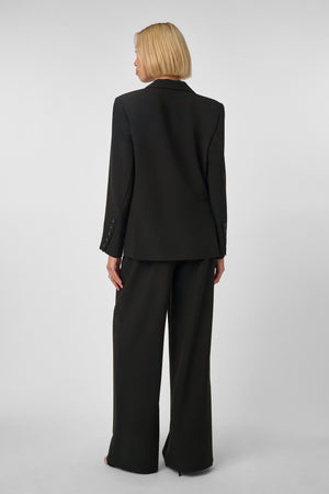 Woman wearing a black oversized suit on a light gray background